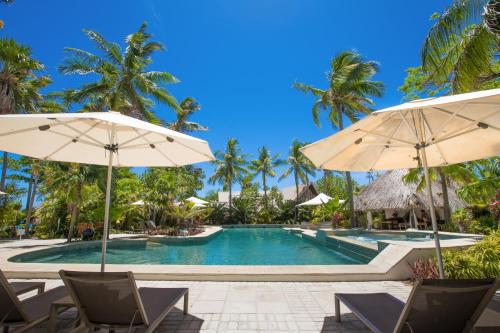 a swimming pool with umbrellas and chairs and palm trees at Castaway Island, Fiji in Castaway Island