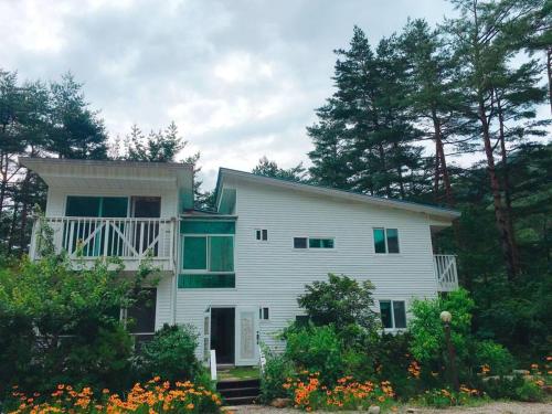 a white house with a balcony and trees and flowers at Blue Sky Milky Way Pension in Yangyang