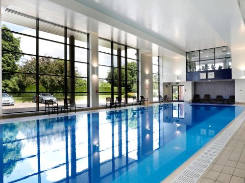 a swimming pool with blue water in a building with windows at Macdonald Alveston Manor Hotel & Spa in Stratford-upon-Avon