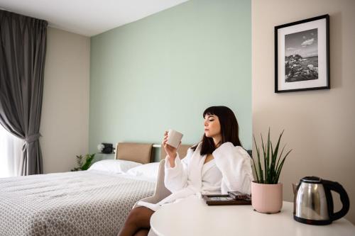 a woman sitting on a bed holding a cup of coffee at Alma Suites in Naples