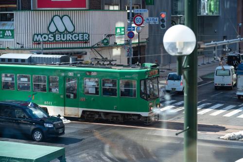 a green train on a city street with cars at THE KNOT SAPPORO in Sapporo