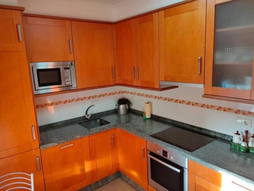 a kitchen with wooden cabinets and a sink and a microwave at Precioso piso al lado de las playas en Portonovo in Sanxenxo
