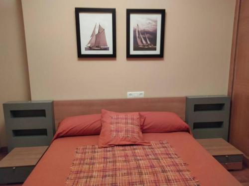 a bed with a red pillow and pictures on the wall at Precioso piso al lado de las playas en Portonovo in Sanxenxo