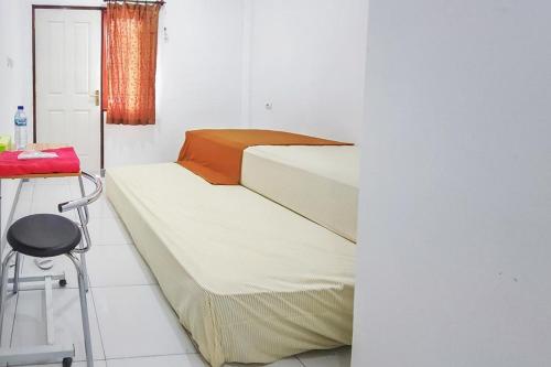 2 camas en una habitación blanca con taburete en Shekinah Homestay & Cafe Waikabubak Mitra RedDoorz, en Waikabubak