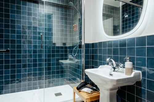 y baño de azulejos azules con lavabo y ducha. en Edgar Suites Montmartre - Abbesses, en París