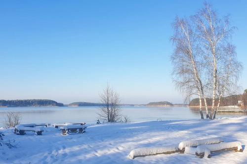 a snow covered field with picnic tables in front of a lake at Zakątek Borsk, Jasnochówka 2, domek 37 in Borsk