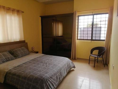 a bedroom with a bed and a chair and a window at Cheerful 2-bedroom Apartment with free parking in Kumasi