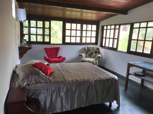 Schlafzimmer mit einem Bett mit einem roten Stuhl und Fenstern in der Unterkunft CASA SURYA, Piscina Fantástica, Churrasqueira, Completa, 18 HÓSPEDES na REGIÃO DOS LAGOS - Casa de Campo in Iguaba Grande