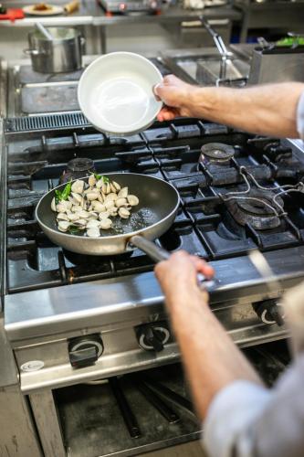 a person cooking food in a pan on a stove at La Tonnara di Bonagia Resort in Valderice