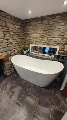 a large white bath tub in a room with a stone wall at Log Burner 3 double bedroom very cosy in Kendal