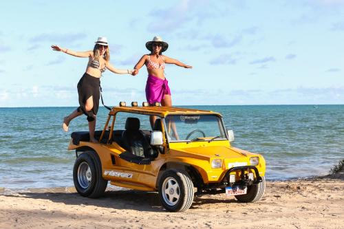 two women standing on top of a yellow jeep on the beach at Pousada Orla dos Corais in Maragogi