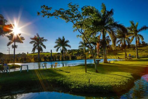 a pool with palm trees and the sun shining at Quatro Estações Pesqueiro e Hotel Fazenda in Esmeraldas