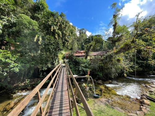 eine Holzbrücke über einen Fluss mit einem Haus im Hintergrund in der Unterkunft Chalé Truta da Floresta in Visconde De Maua