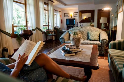 a woman reading a book on a coffee table in a living room at Hotel Infantado in Ojedo