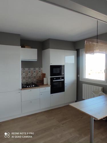 a kitchen with white cabinets and a black microwave at appartement belle vue in Courseulles-sur-Mer