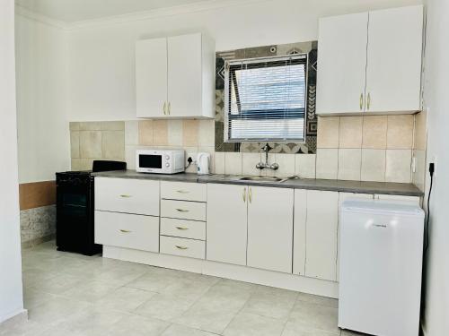 a kitchen with white cabinets and a sink and a microwave at Airport Doozy Guest House in Kempton Park