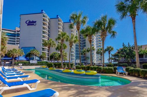 a resort with a swimming pool with lounge chairs and palm trees at Carolina Winds in Myrtle Beach