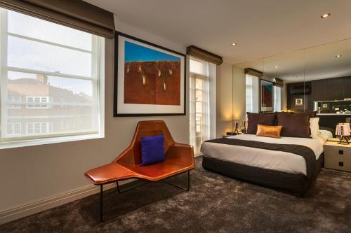 Schlafzimmer mit einem Bett, einem Stuhl und Fenstern in der Unterkunft Quest East Melbourne in Melbourne