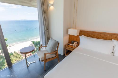 a hotel room with a bed and a chair and the ocean at Chicland Boutique Danang Beach Hotel in Da Nang