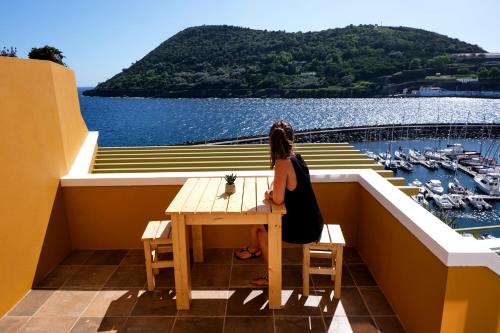 a woman sitting at a table on a balcony overlooking the water at Mid-Atlantic Boutique Hostel in Angra do Heroísmo