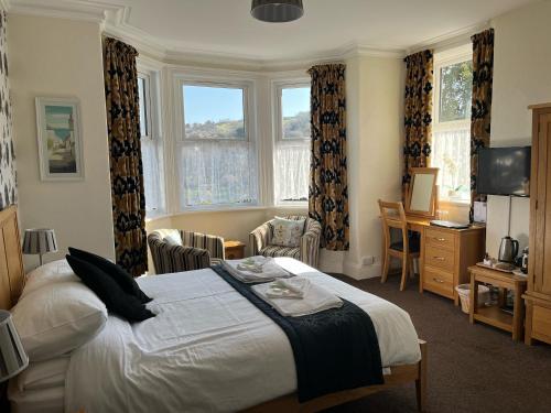 a bedroom with a bed and a desk and windows at Cairn House in Ilfracombe
