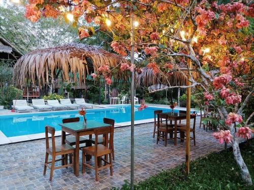 una mesa y sillas bajo una sombrilla de paja junto a una piscina en La Habana Amazon Reserve, en Puerto Maldonado