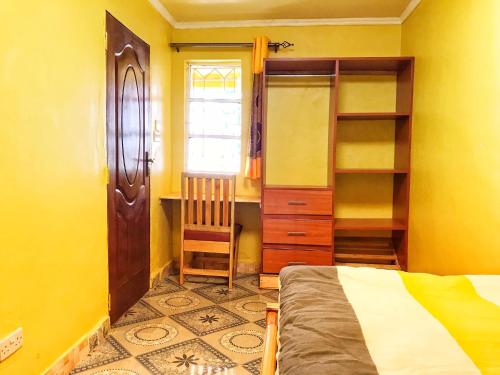 1 dormitorio con paredes amarillas, 1 cama y escritorio en The Swiss Side Iten en Iten
