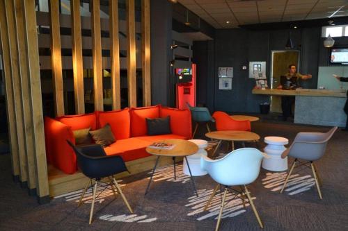 a room with an orange couch and tables and chairs at ibis Bordeaux Lac in Bordeaux