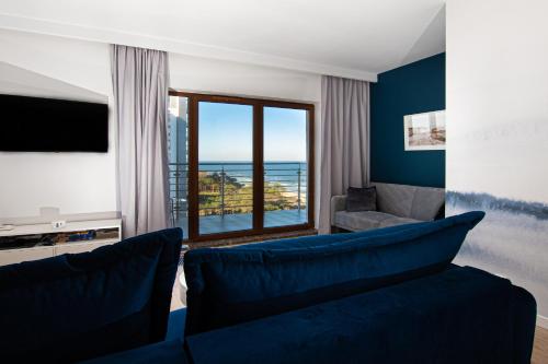 a living room with a blue couch and a large window at Apartament Baltic Sea Gate Porta Mare 55m2 in Dziwnówek