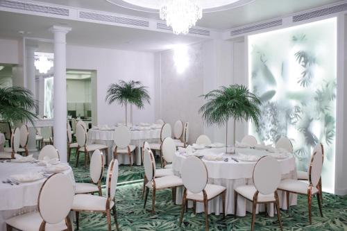 a room with white tables and chairs and palm trees at Hotel Relax Craiova in Craiova