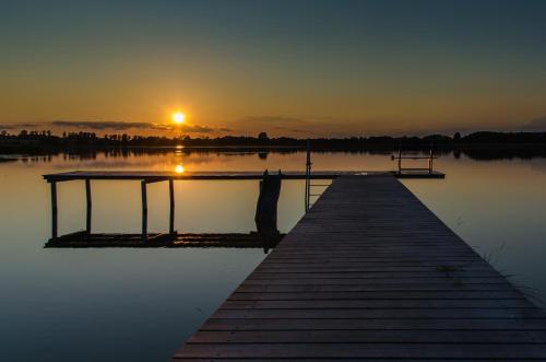 a dock on a lake with the sunset in the background at Siedlisko Miluki - Apartamenty nad Jeziorem z Jacuzzi & Sauną in Ełk