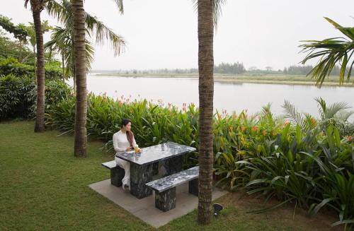 a man sitting on a bench next to a lake at THE VILLA @ RED BRIDGE in Hoi An