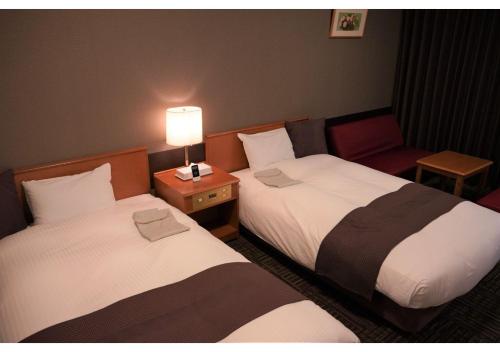 two beds in a room with a lamp and a chair at Hotel Hachiman in Hachiman