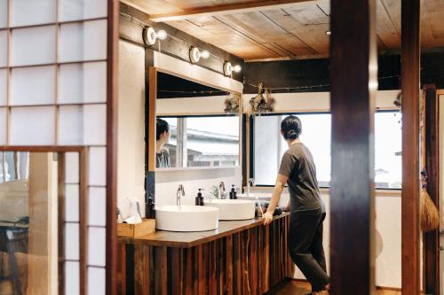 a man standing at a bathroom counter with a sink at Yamairo guesthouse in Iida