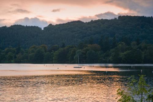 a beach with a boat in the water at sunset at Macdonald Old England Hotel & Spa in Bowness-on-Windermere