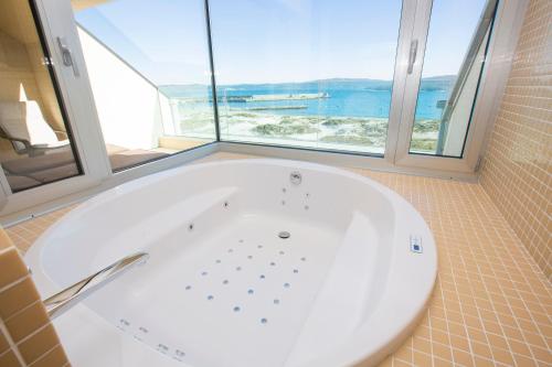 a bath tub in a bathroom with a large window at Hotel Boutique O Náutico Laxe in Laxe
