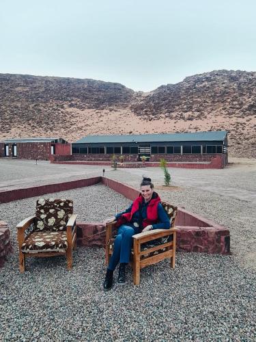 a man sitting on a bench next to two chairs at Shakria Bedouin Life Camp in Wadi Rum
