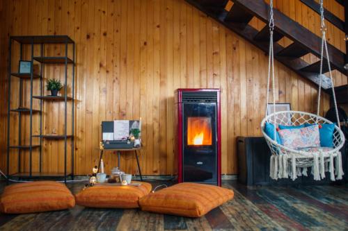 Habitación con pared de madera, chimenea y almohadas de color naranja. en The Wooden Nest -Covasna en Covasna