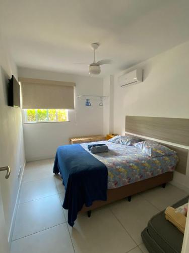 a bedroom with a bed with a blue blanket and a window at APARTAMENTO EM ARRAIAL DO CABO - RJ in Arraial do Cabo