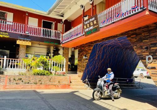 a man riding a scooter in front of a building at Shin Sane Guest House in Mae Salong