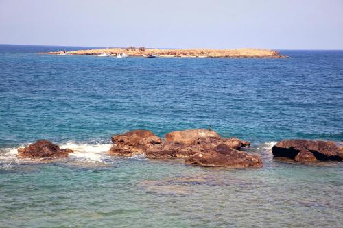 a group of rocks in the water with an island in the background at THALIA APARTMENTS CHANlA in Chania