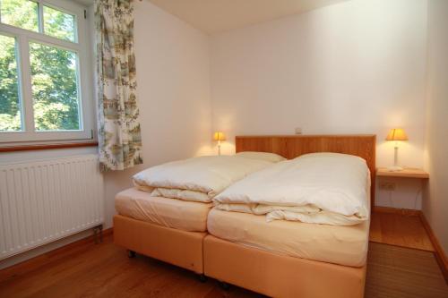 a bedroom with a bed with white sheets and a window at Gut Settin am See - Ferienhäuser in Settin