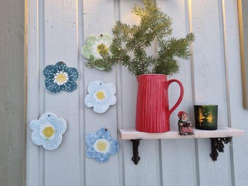 a red vase on a shelf with flowers on a wall at T-R Huset i Hellosan in Bøstad