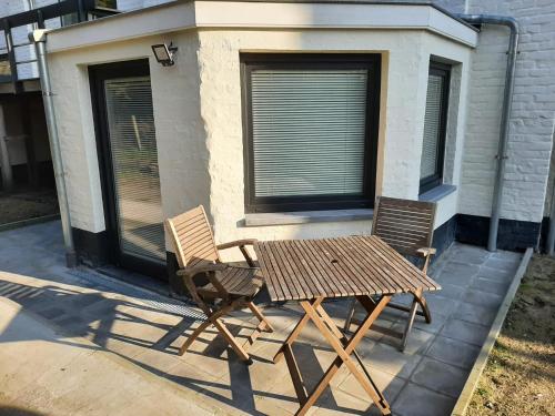 a wooden table and two chairs in front of a building at Oostduinkerke aan zee vakantiewoningen De Baeken in Koksijde