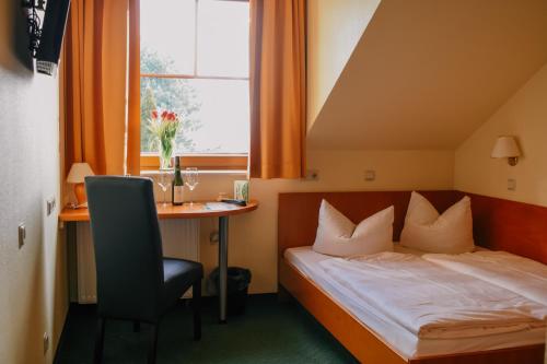 a bedroom with a bed, desk, chair and window at Landhotel Dresden in Dresden