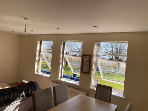 uma sala de jantar com 3 janelas e uma mesa e cadeiras em Sea-view flat near Mumbles. em Swansea