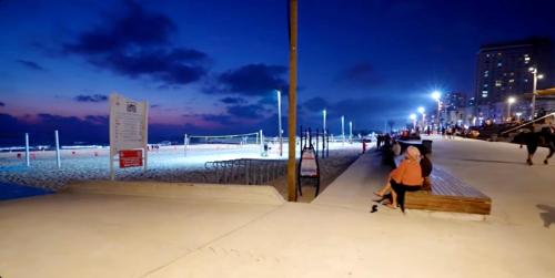 a woman sitting on a bench at the beach at night at Hotel Apartment Short Term Tel Aviv Bat Yam 5 in Bat Yam