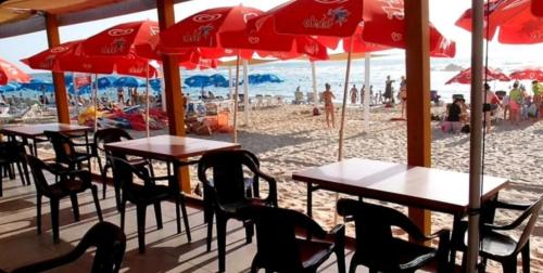 a beach with tables and chairs and red umbrellas at Hotel Apartment Short Term Tel Aviv Bat Yam 5 in Bat Yam