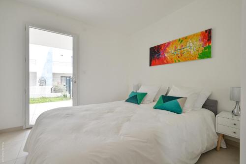 a white bedroom with a large white bed with green pillows at T2 NEUF A4 RDJ-PISCINE–ACCÈS DIRECT PLAGES ET CENTRE VILLAGE– in Saint-Cyr-sur-Mer