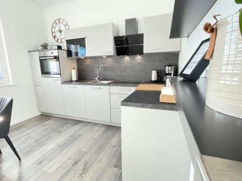a kitchen with white cabinets and a black counter top at Lee-Moderne Neubauwohnung in Strandnähe - Wallbox in Wremen